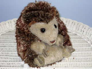 A plush hedgehog toy with brown and beige fur sits on a white wicker surface against a light blue background.